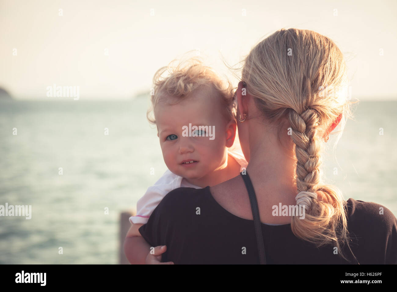 Enfant avec un regard sincère étreindre sa mère assis sur ses mains et en regardant la caméra. Mère tenant son bébé et à la recherche dans la distance vers Banque D'Images