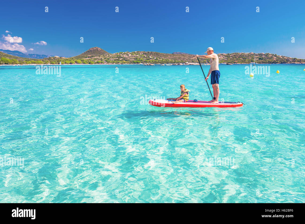 Père heureux avec son petit fils s'amusant sur le stand up paddle board sur l'île de Corse, France. Banque D'Images