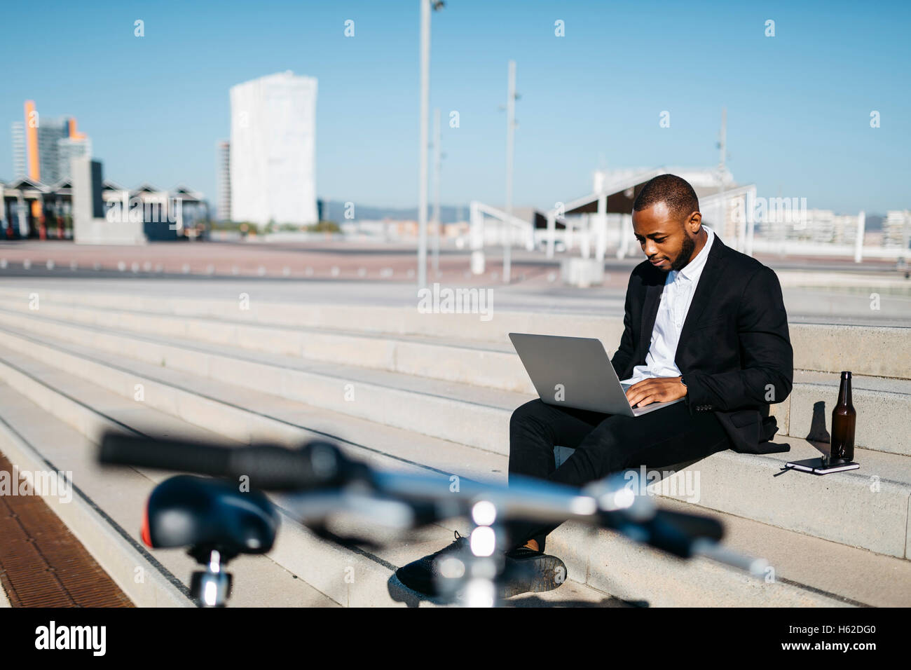 Businessman sitting on stairs avec bouteille de bière using laptop Banque D'Images