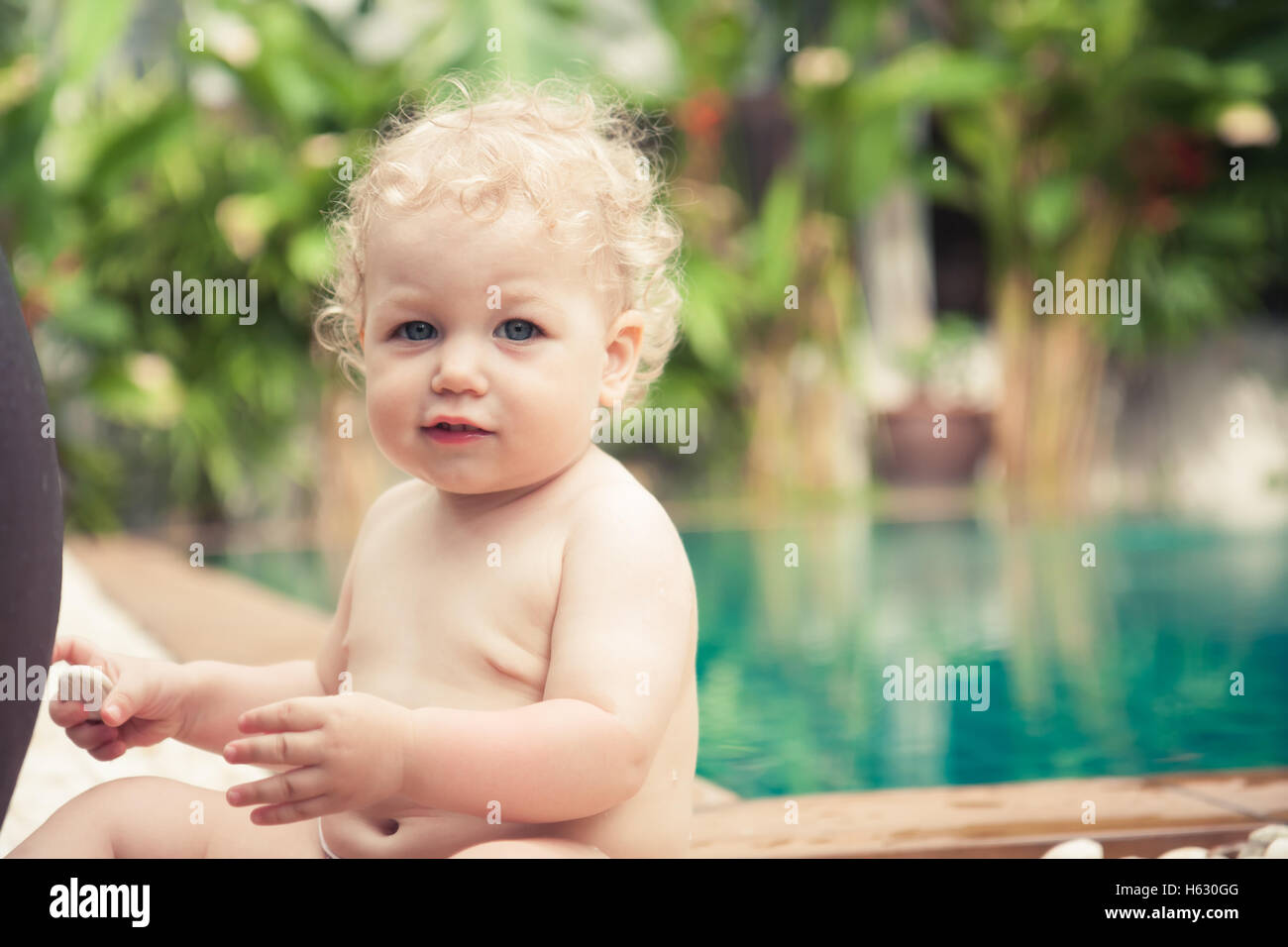 Cute little baby sitting in front of swimming pool looking at camera lors des vacances d'with copy space Banque D'Images
