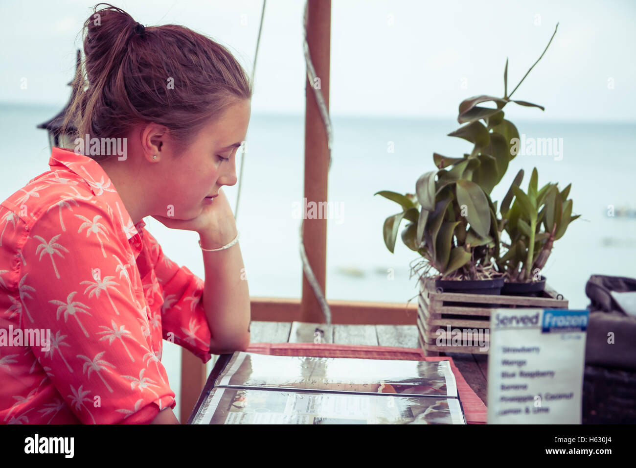 Jeune femme étudie un menu dans un café sur la plage tout en vacances avec copie espace. Banque D'Images