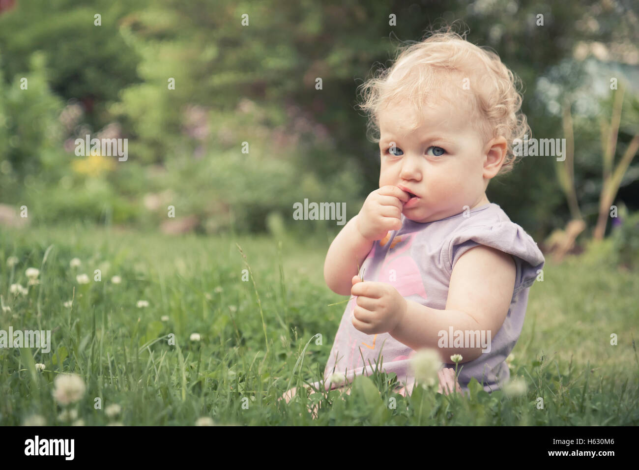 Cute baby girl sitting in grass parmi les fleurs fleurissent en été park with copy space Banque D'Images