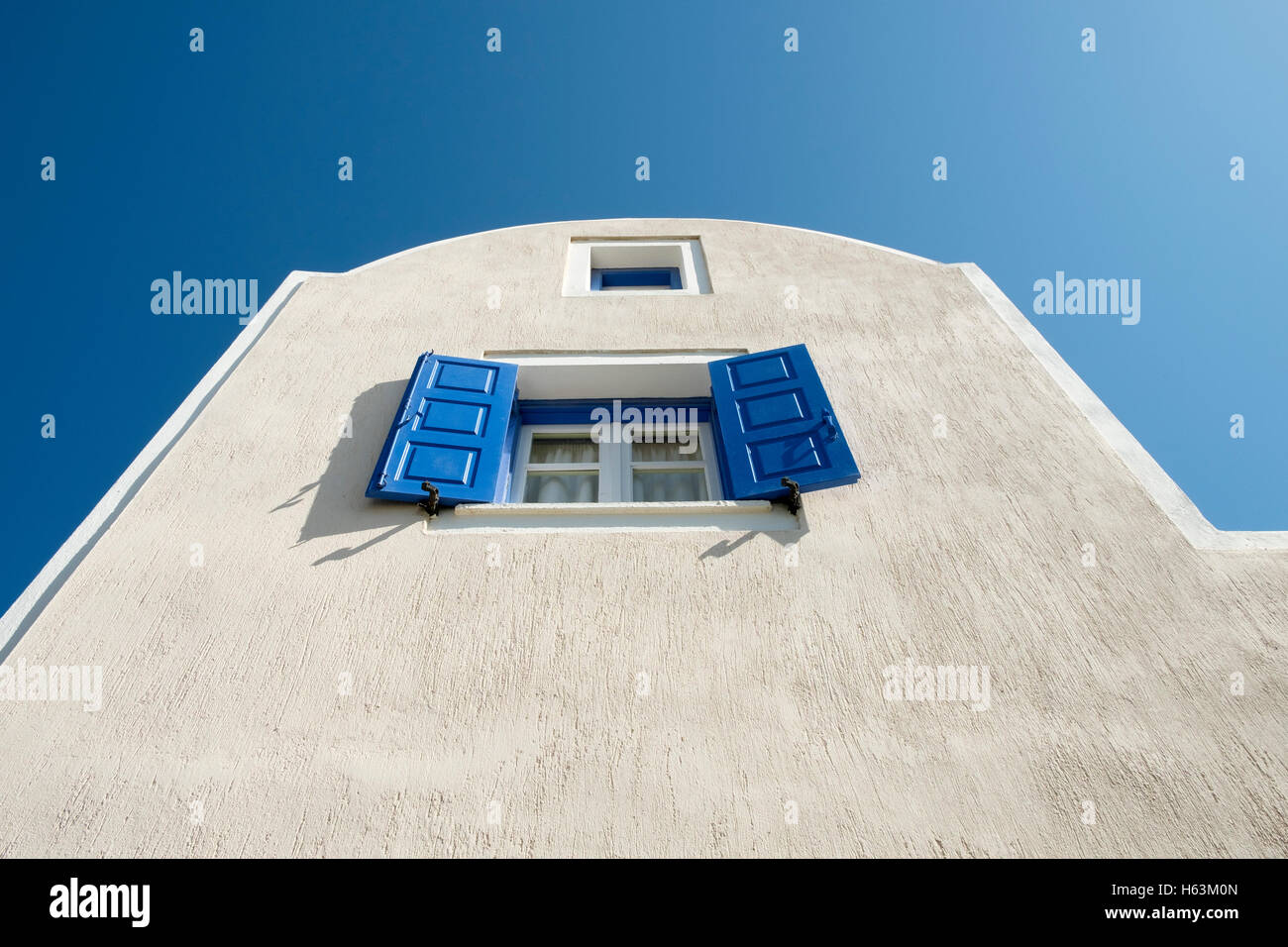 Des volets bleus sur la fenêtre d'un bâtiment blanc sur fond de ciel bleu sur Santorin, Grèce. Banque D'Images