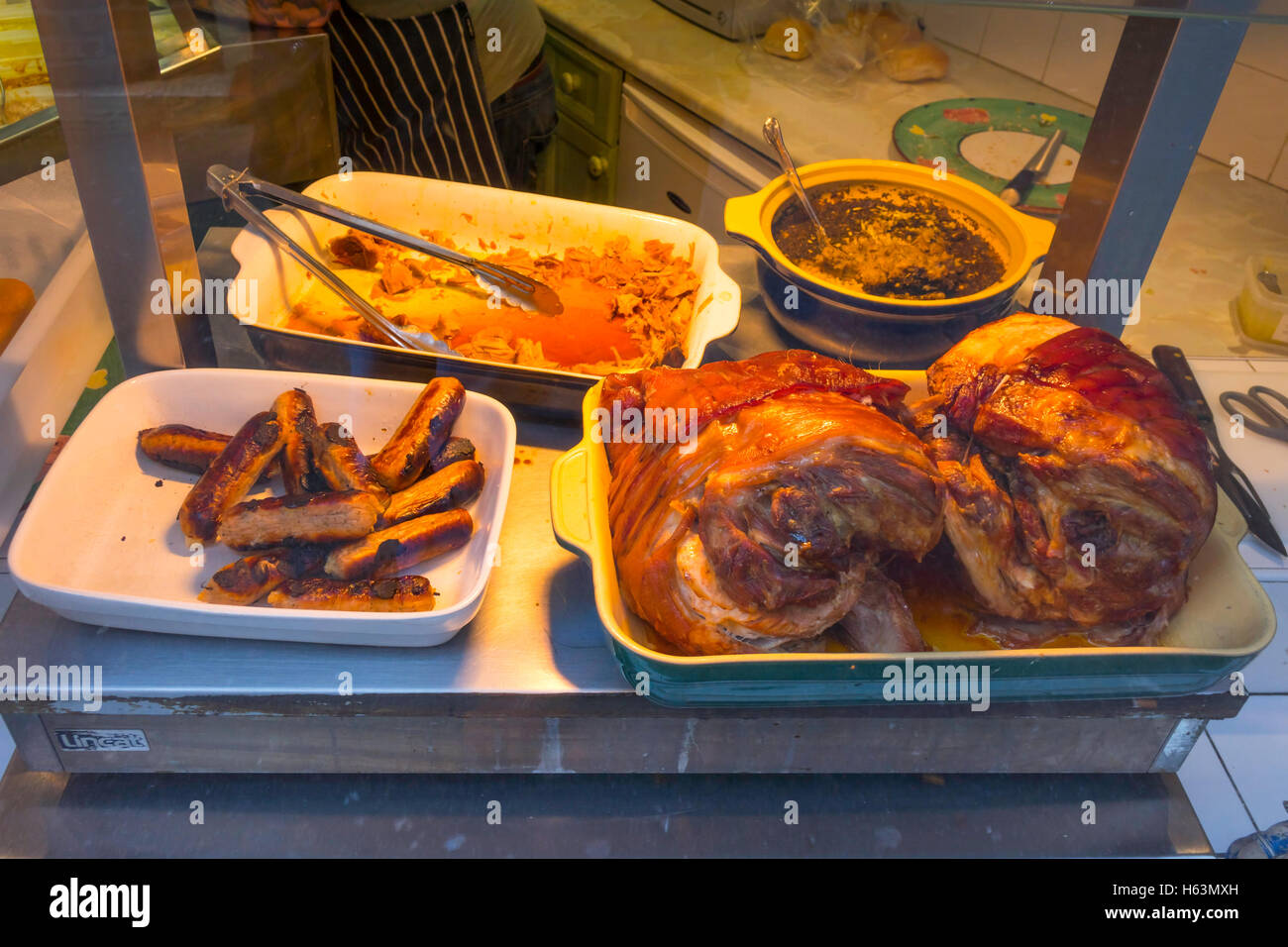 Les joints fraîchement rôtis de viande de porc et saucisses dans une vitrine de la vente de sandwichs chauds. Banque D'Images