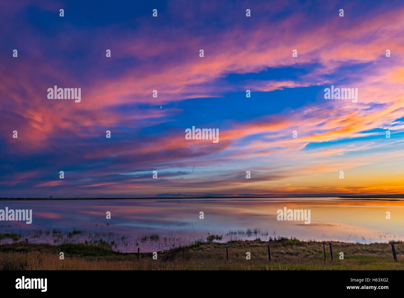 Coucher du soleil sur les couleurs Deadhorse Lake dans le sud de l'Alberta, le 8 juillet 2016. La lune croissante brille au milieu de l'étang du grand birieux Banque D'Images