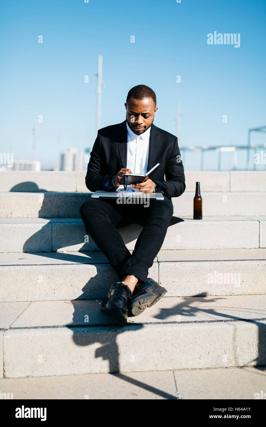 Businessman sitting on stairs avec bouteille de bière, ordinateur portable et ordinateur portable Banque D'Images