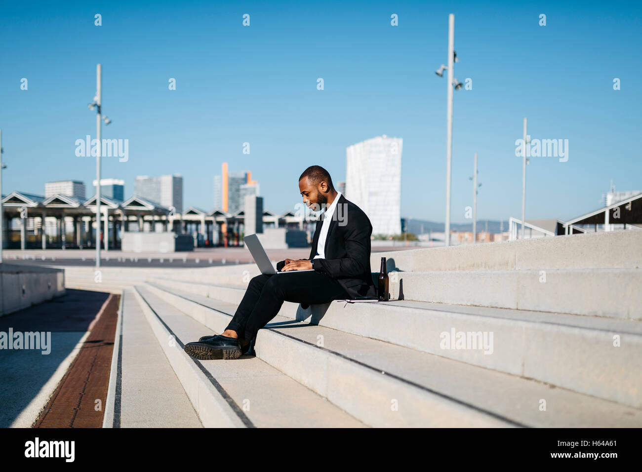 Businessman sitting on stairs avec bouteille de bière using laptop Banque D'Images