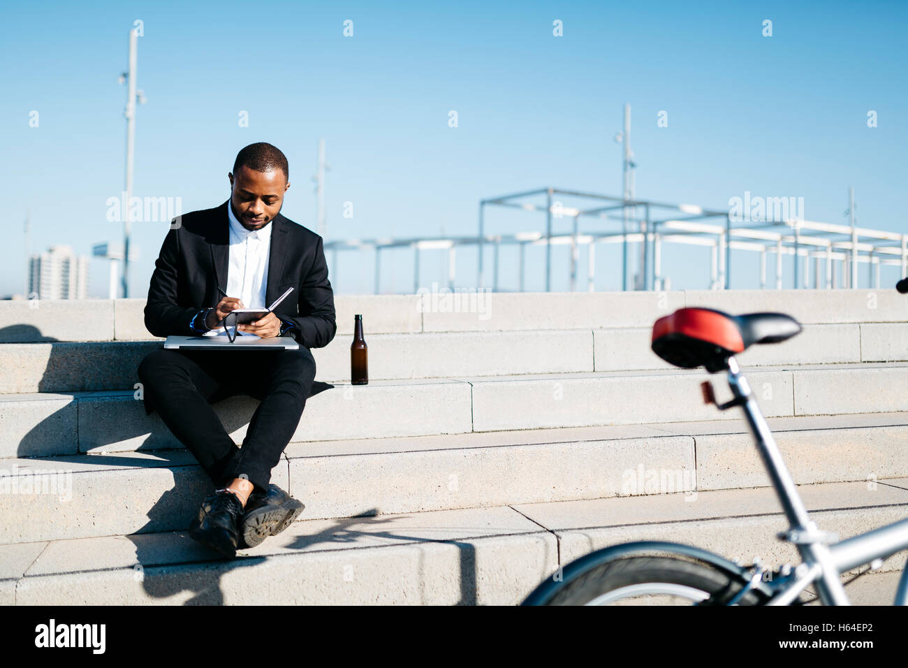Businessman sitting on stairs avec bouteille de bière, ordinateur portable et ordinateur portable Banque D'Images
