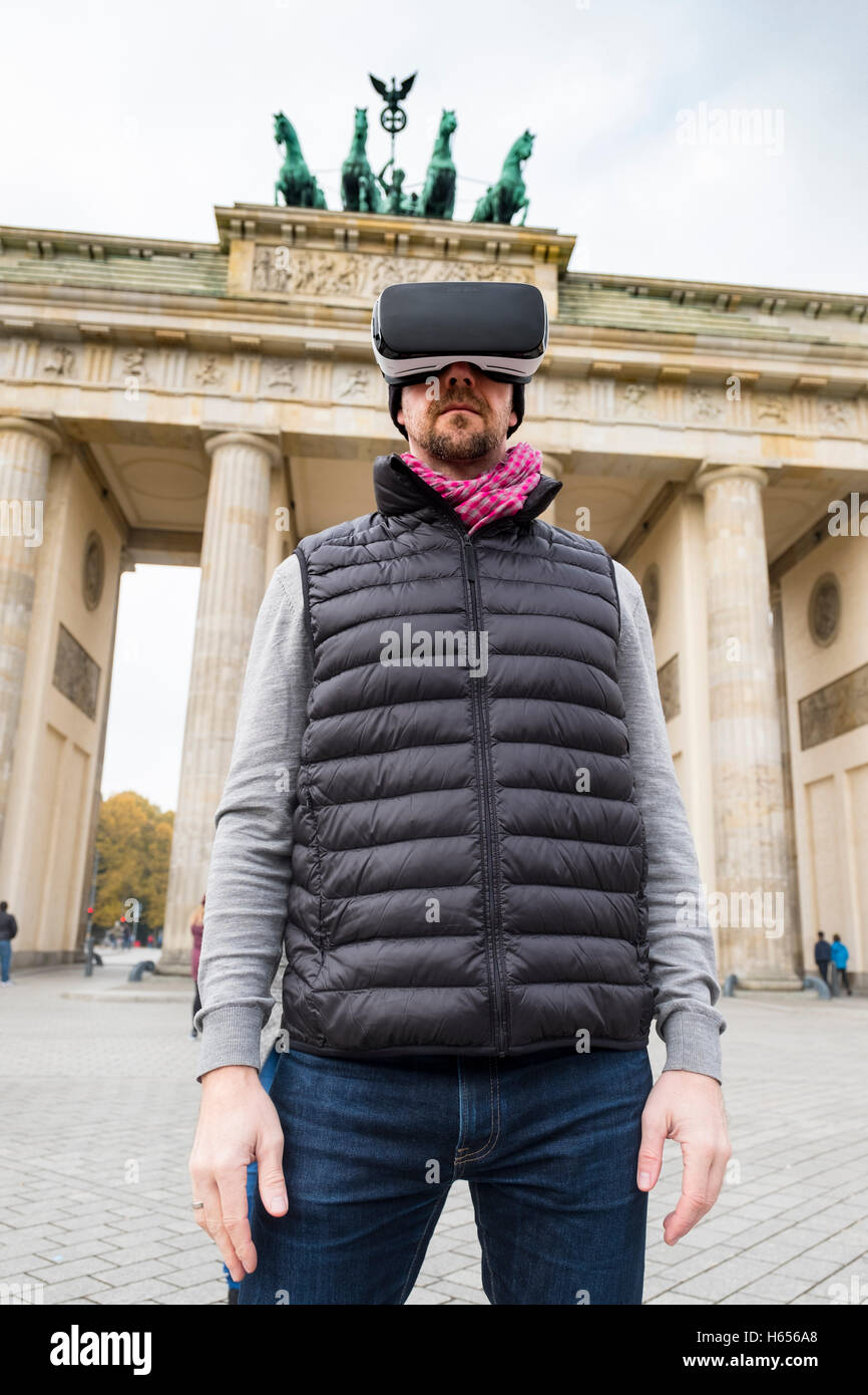 Homme portant la Réalité Virtuelle (RV) nocturne en face de la porte de Brandebourg à Berlin, Allemagne Banque D'Images