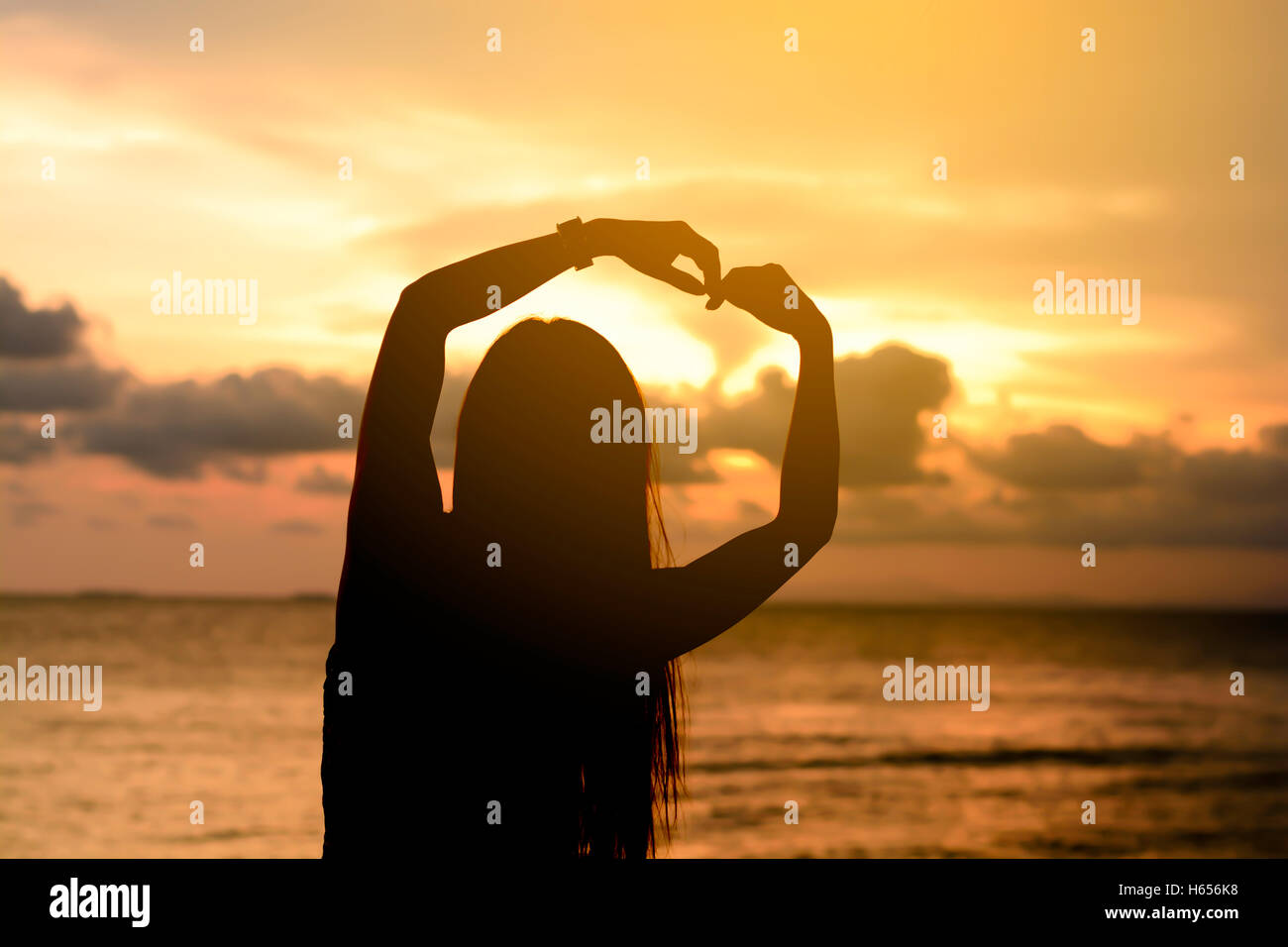Femme mains formant un cœur avec sunset silhouette Banque D'Images