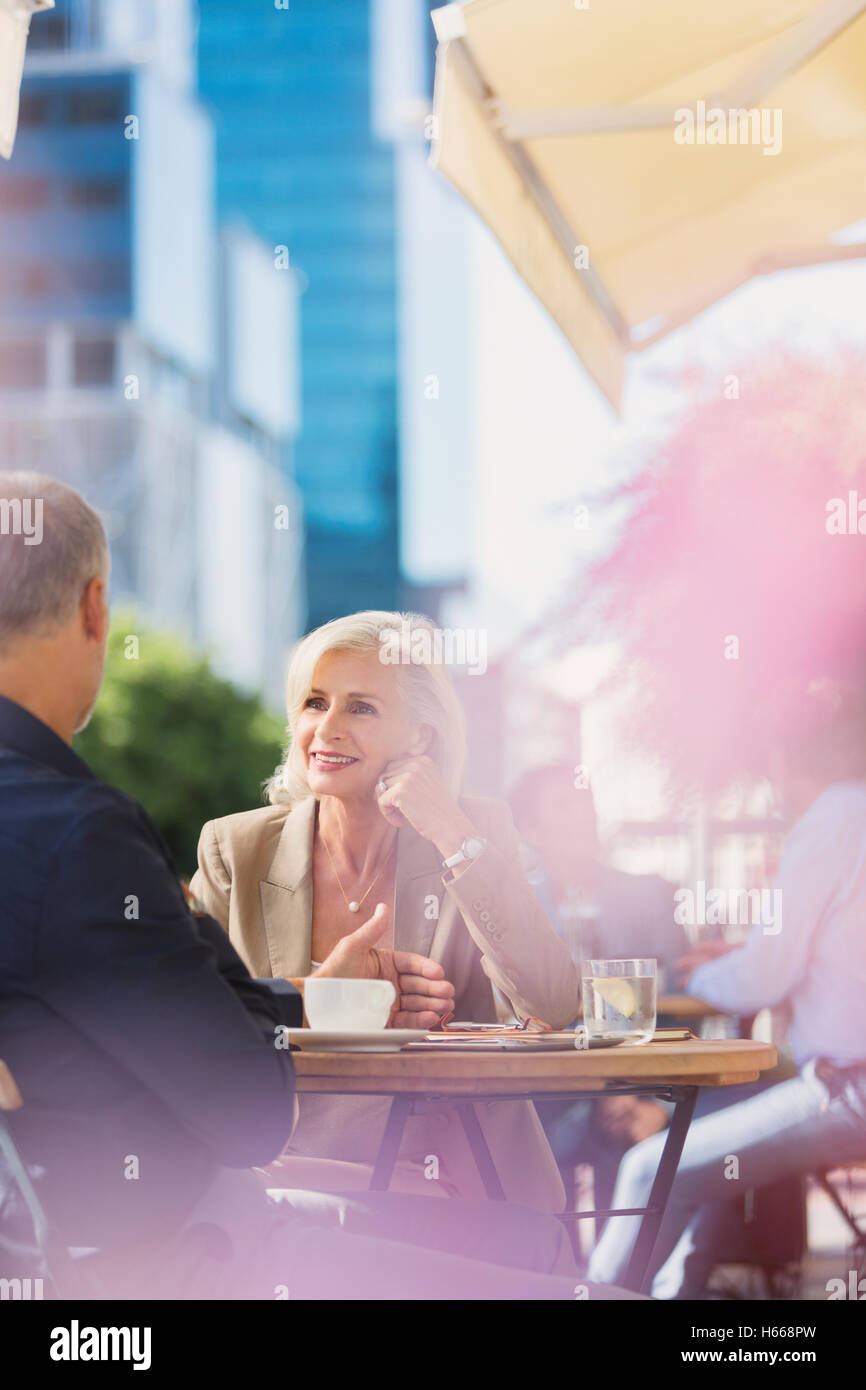 Businesswoman listening to businessman at sunny urban sidewalk cafe Banque D'Images