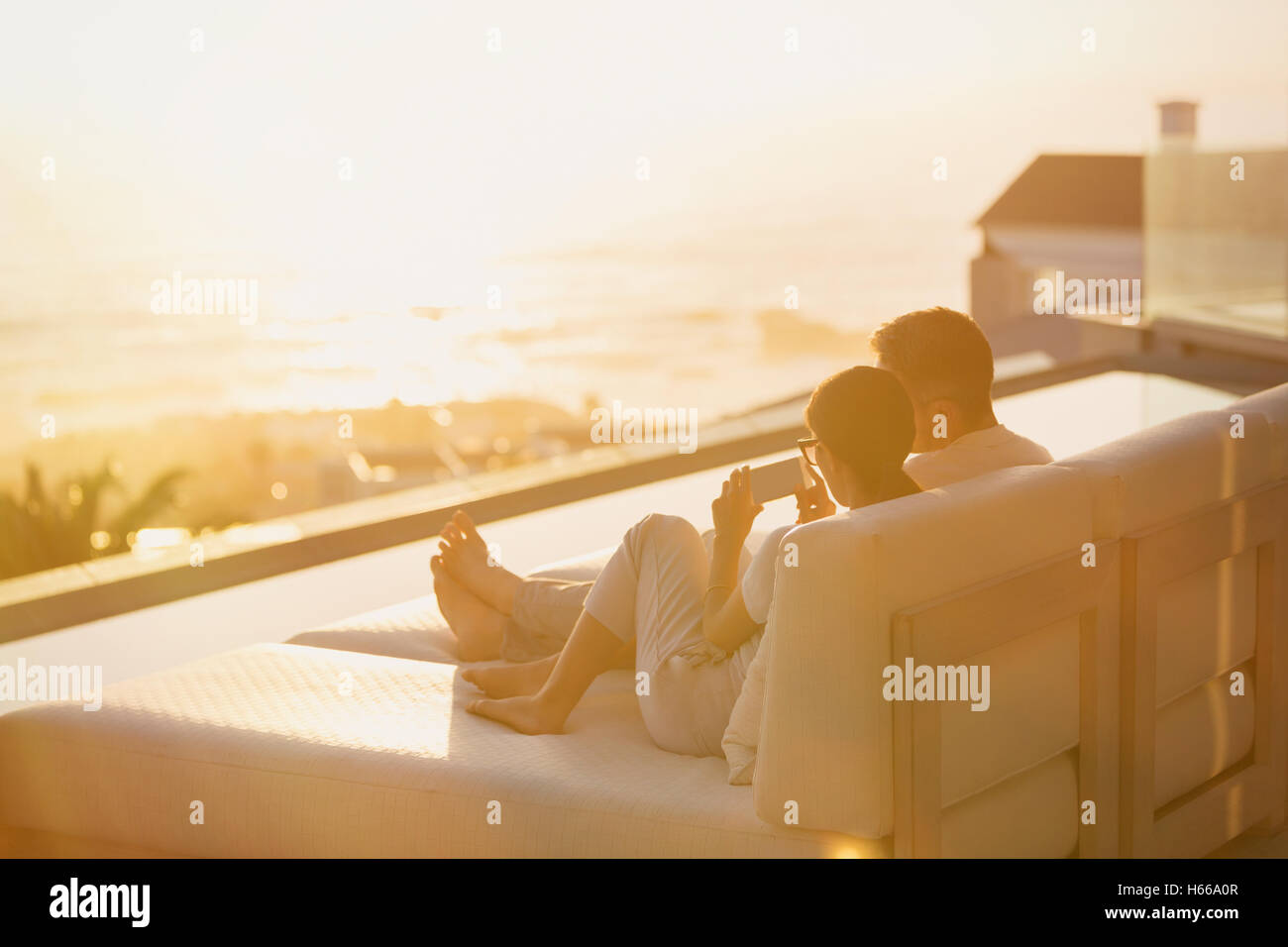 Silhouette couple using cell phone on chaise longue avec coucher du soleil sur l'océan Banque D'Images