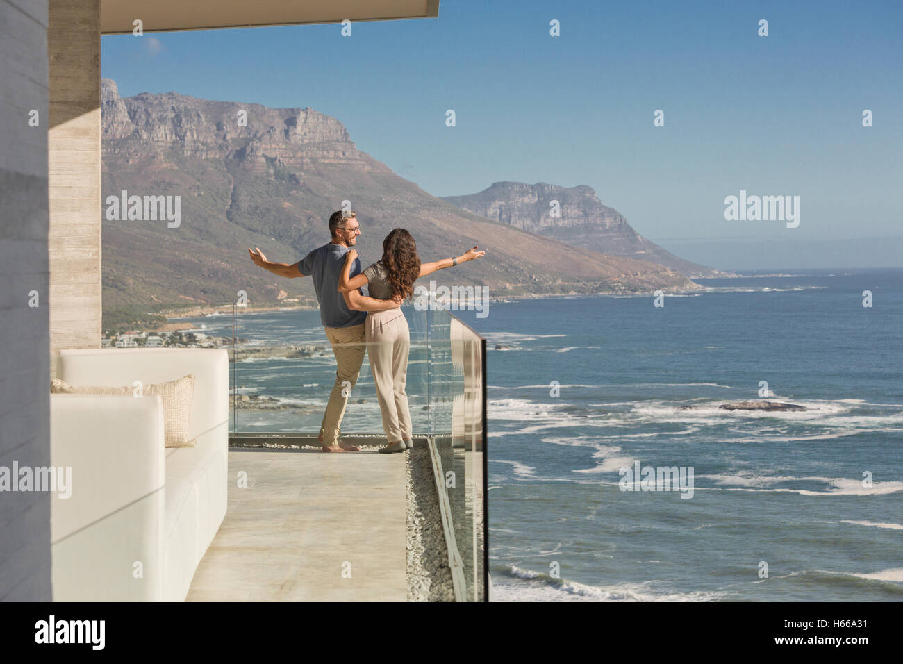Carefree couple standing on sunny luxe balcon donnant sur l'océan et sur la montagne Banque D'Images