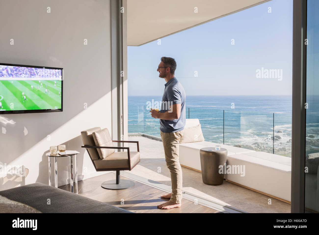 Homme regarder le soccer sur plat de luxe porte patio avec vue sur l'océan Banque D'Images