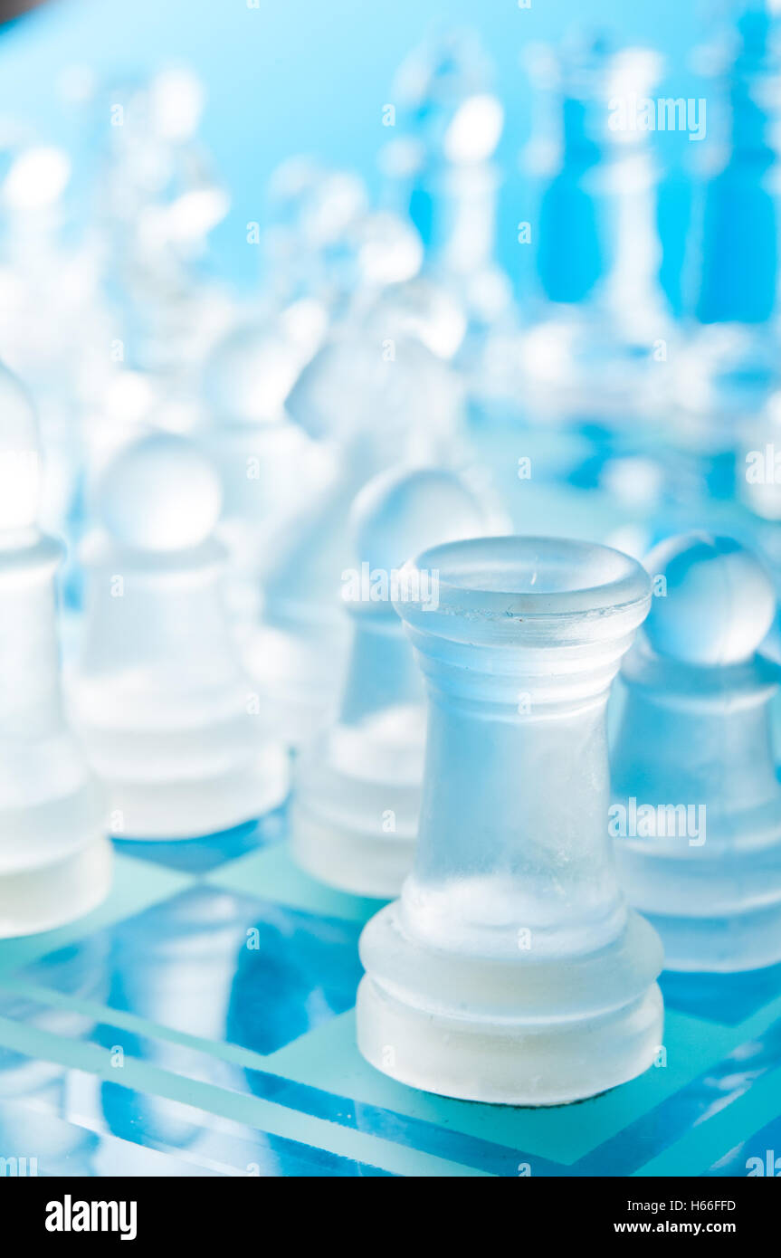 Des pièces d'échecs en verre clair et dépoli s'affrontent sur un échiquier en verre bleu dans une composition studio en gros plan lumineuse Banque D'Images