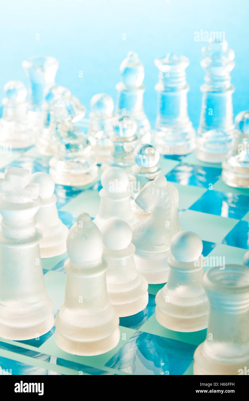 Des pièces d'échecs en verre clair et dépoli s'affrontent sur un échiquier en verre bleu dans une composition studio en gros plan lumineuse Banque D'Images