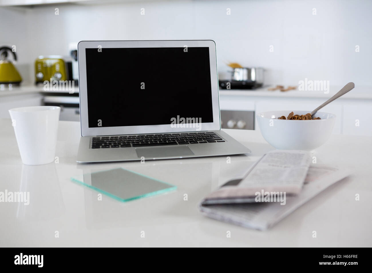 Bol de petit-déjeuner avec café mug, ordinateur portable et de journaux dans la cuisine Banque D'Images