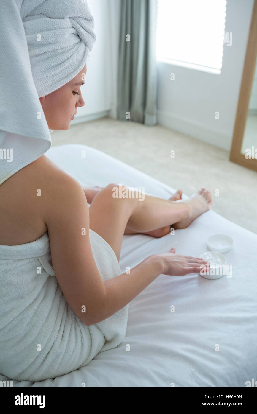 Woman applying moisturizer cream sur sa jambe dans la chambre Banque D'Images