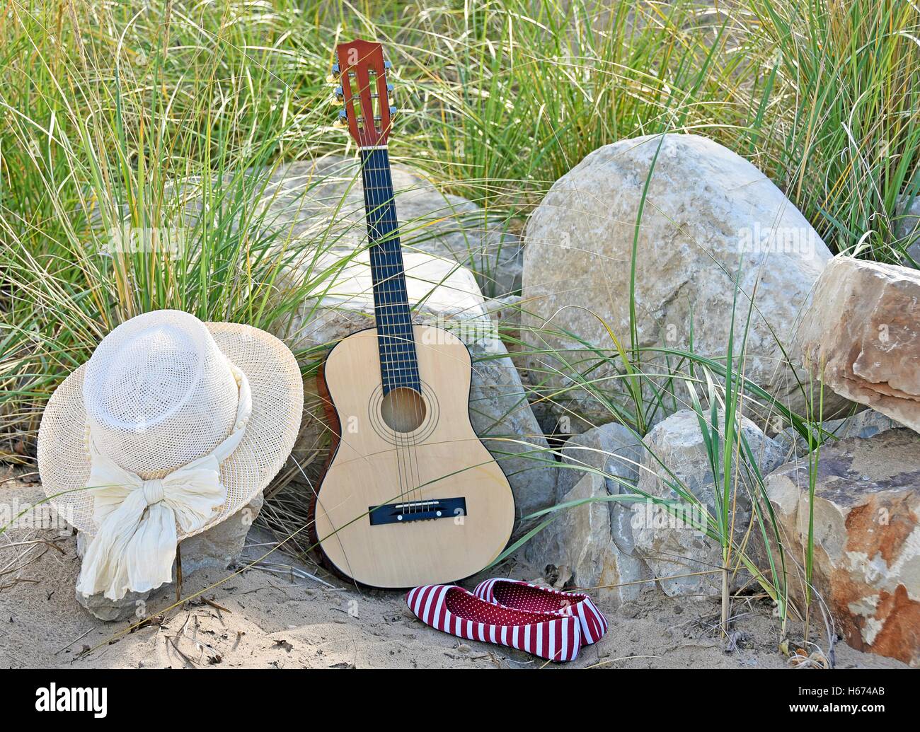 Guitare avec chapeau et rouge et blanc à rayures chaussures dans le sable de la plage et de la roche Banque D'Images