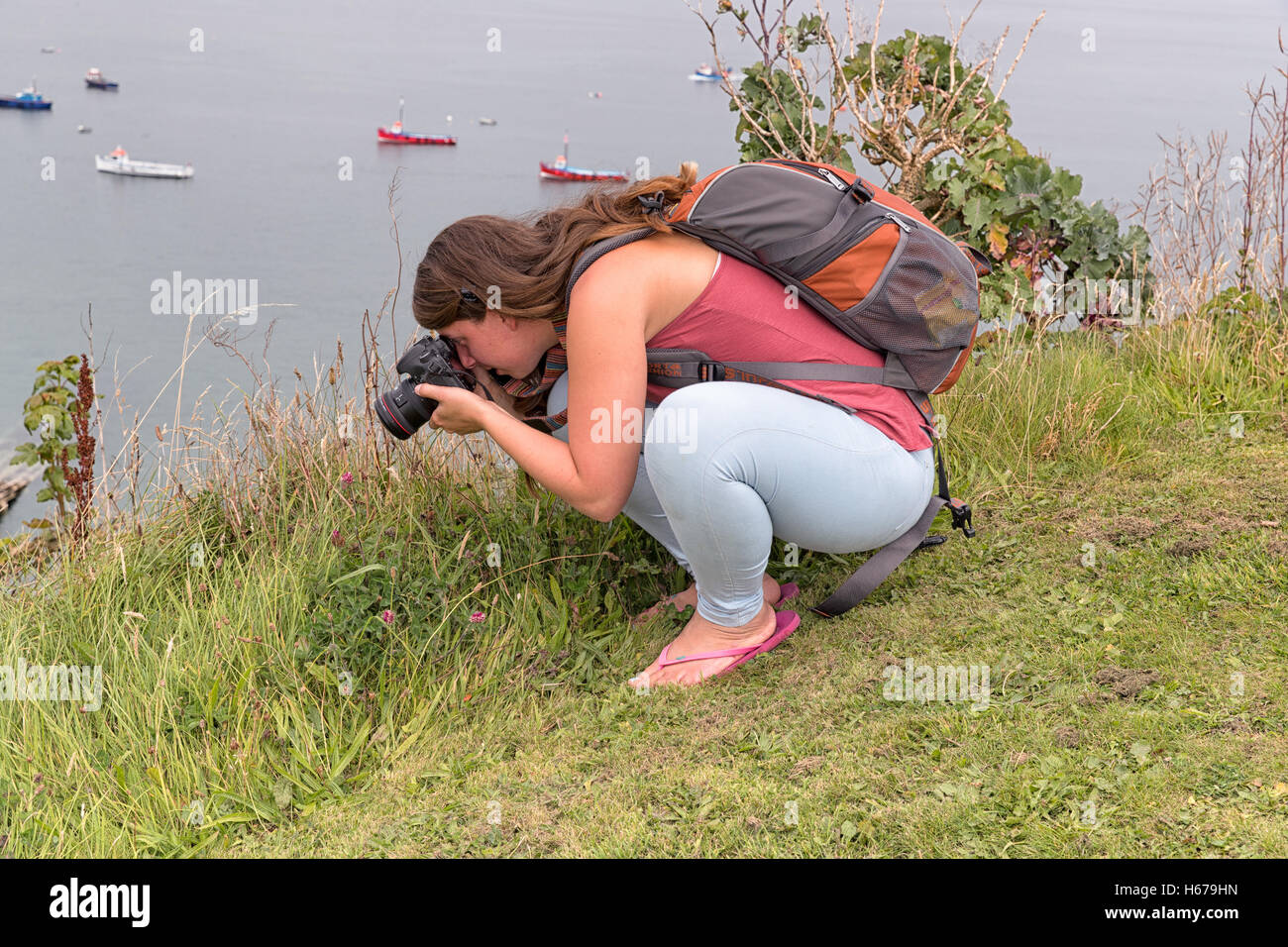 Femme photographe accroupi faisant quelques macro photographie à l'extérieur avec la mer en arrière-plan. Banque D'Images