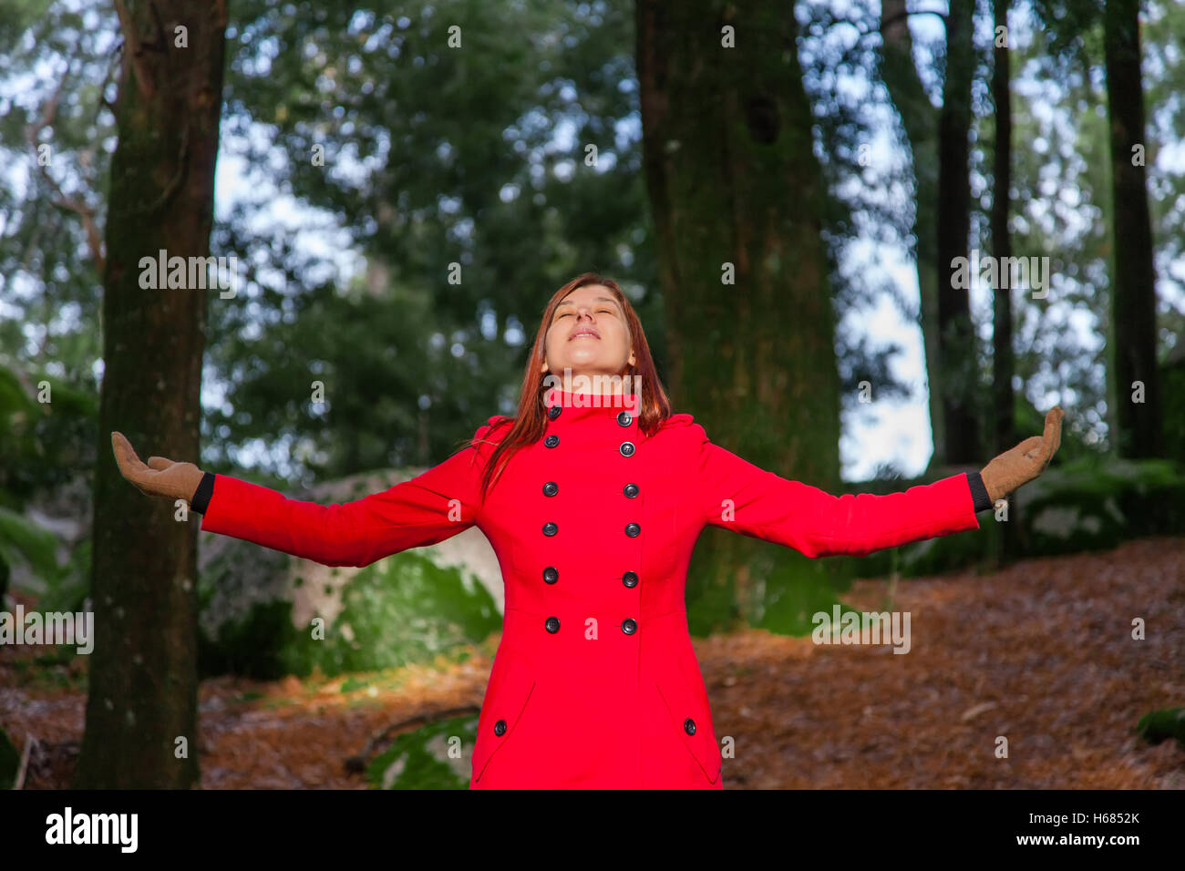 Femme jouissant de la chaleur du soleil d'hiver sur une forêt portant un manteau rouge Banque D'Images