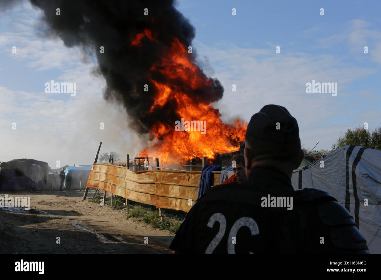 Calais, France. 25 octobre, 2016. Un agent de police watches la cabane brûler. Le deuxième jour de l'expulsion de la Jungle à Calais a vu le démarrage de la démolition de la jungle. Certains refuges ont été démolis par des ouvriers, tandis que d'autres refuges ont été délibérément brûlés. Crédit : Michael Debets/Pacific Press/Alamy Live News Banque D'Images