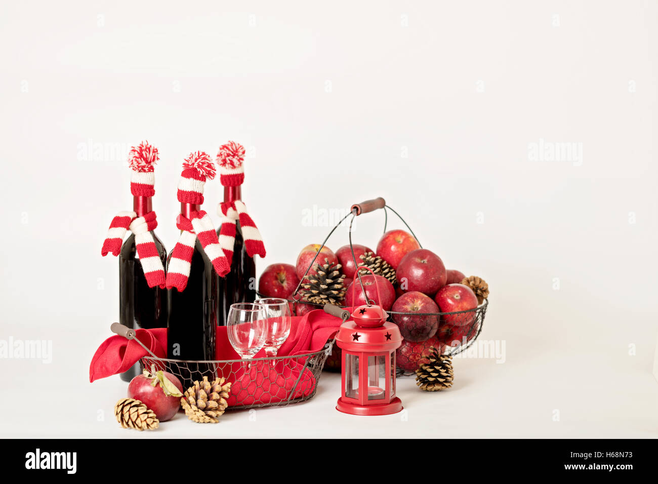 Joyeux Noël et bonne année. Des bouteilles de vin dans un tricot de Santa chapeaux, lunettes et panier de pommes. Banque D'Images