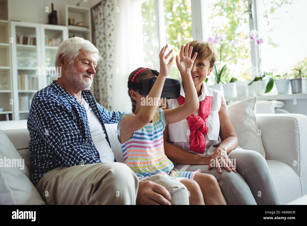 Petite-fille à l'aide de casque de réalité virtuelle avec ses grands-parents dans la salle de séjour Banque D'Images