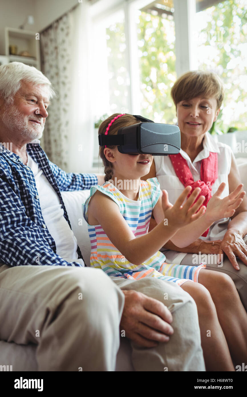 Petite-fille à l'aide de casque de réalité virtuelle avec ses grands-parents dans la salle de séjour Banque D'Images