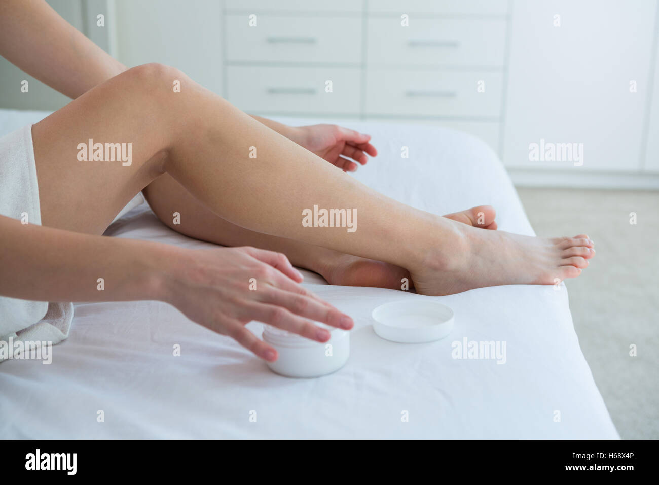 Woman applying moisturizer cream sur sa jambe dans la chambre Banque D'Images