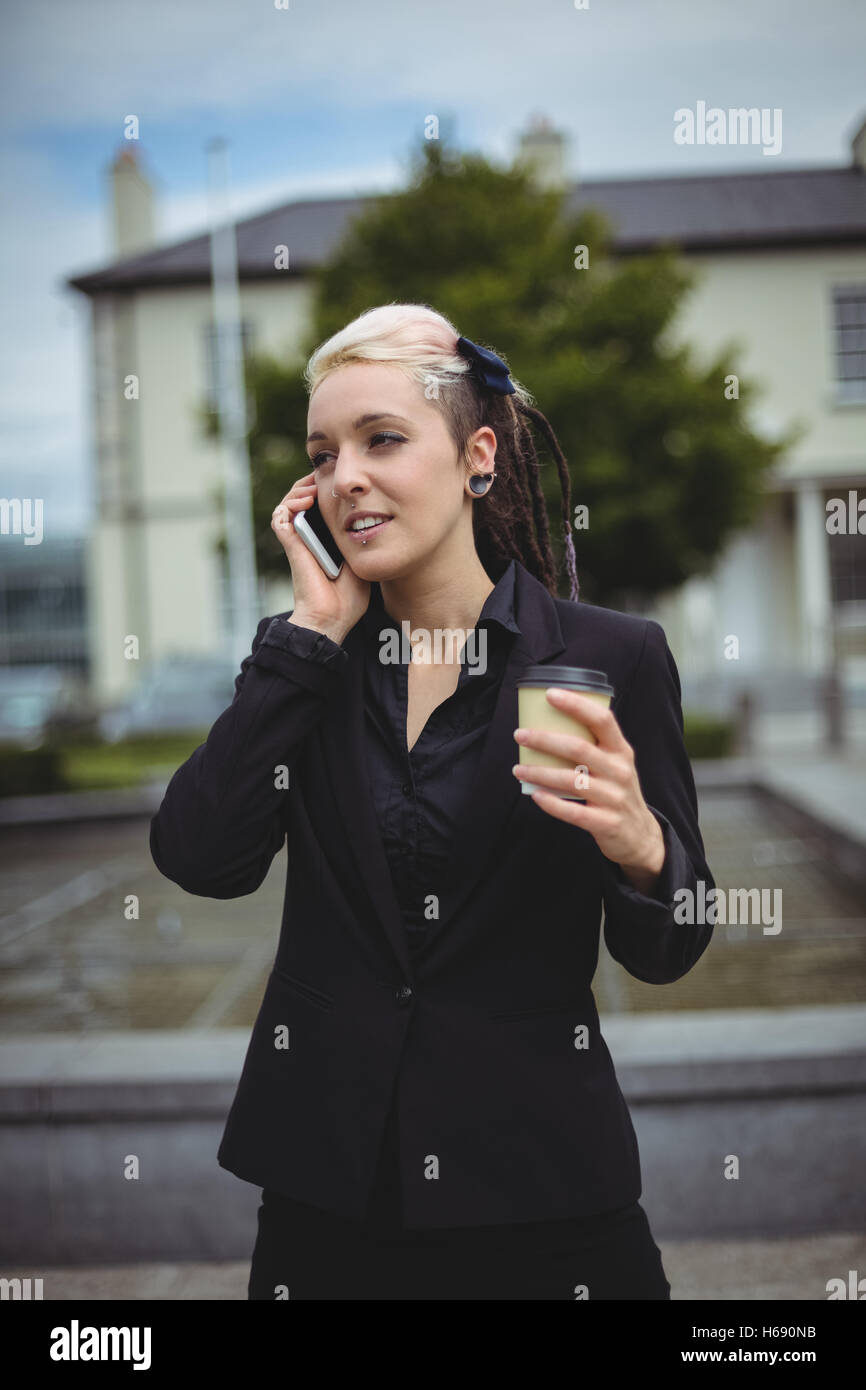 Businesswoman talking on mobile phone tout en tenant la tasse de café à usage unique Banque D'Images