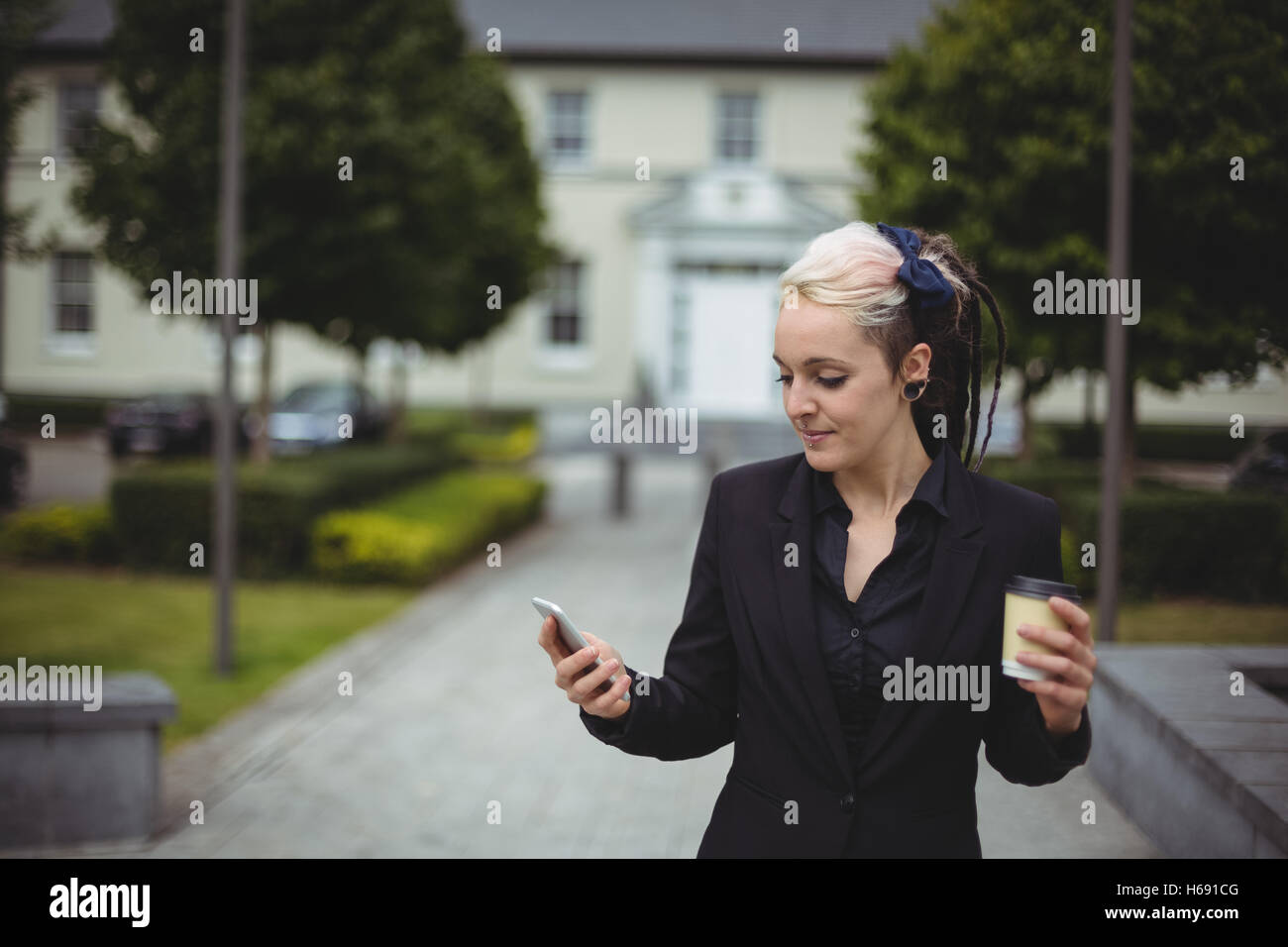 Businesswoman using mobile phone tout en tenant la tasse de café à usage unique Banque D'Images