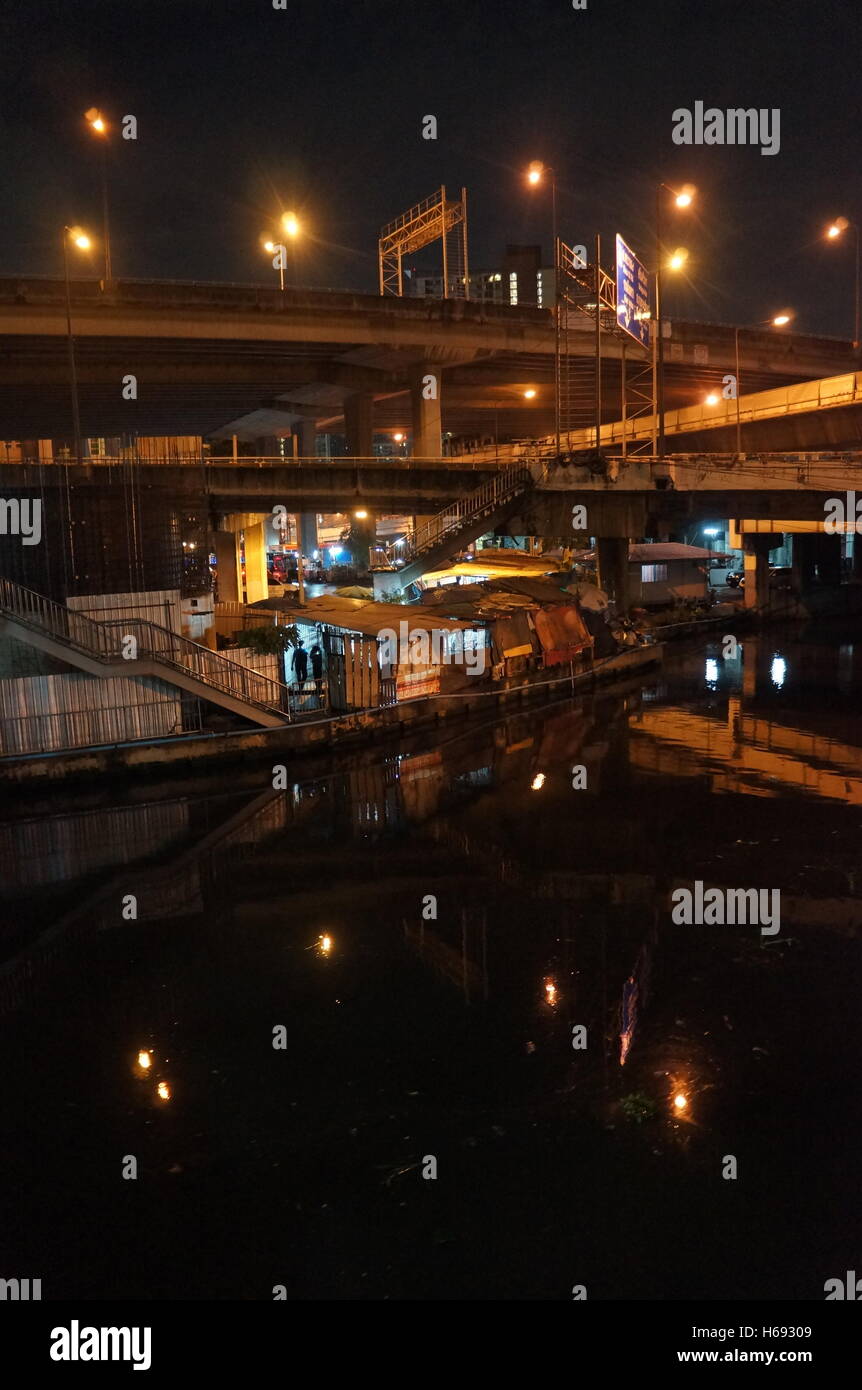 Un bidonville sous plusieurs routes dans le district de l'écrou, Bangkok, Thaïlande, le long de la rivière pendant la nuit. Banque D'Images