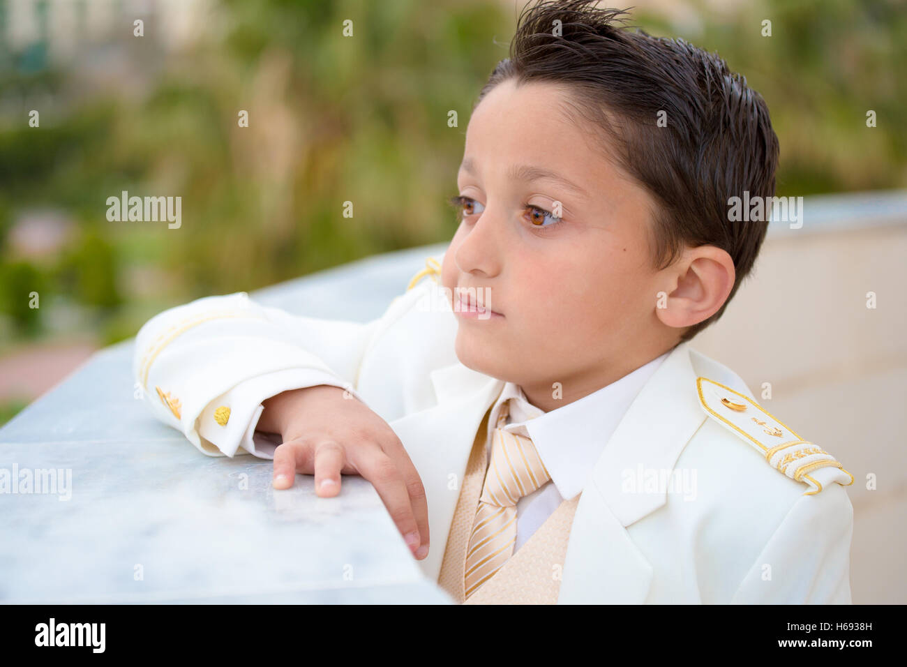 Jeune garçon avec costume blanc s'appuyant sur un mur dans sa Première Communion. Profondeur de champ. Banque D'Images