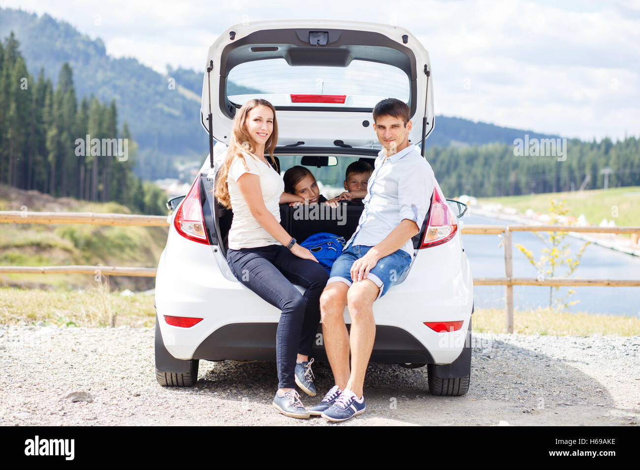 Young family sitting in car trunk se reposant après voyage en montagne Banque D'Images