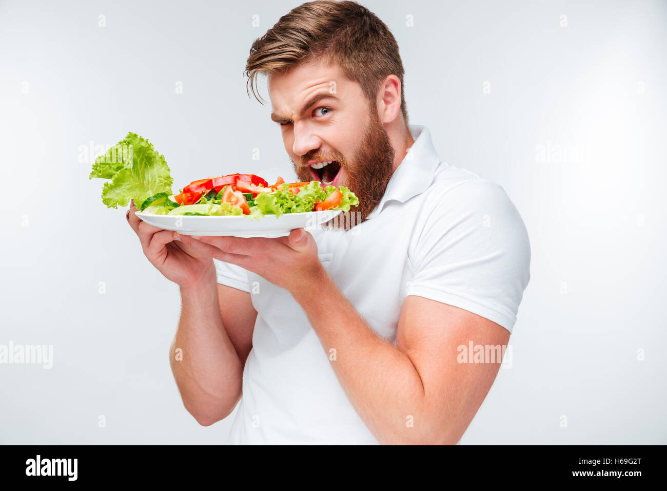 Jeune homme barbu faim salade manger isolé sur fond blanc Banque D'Images