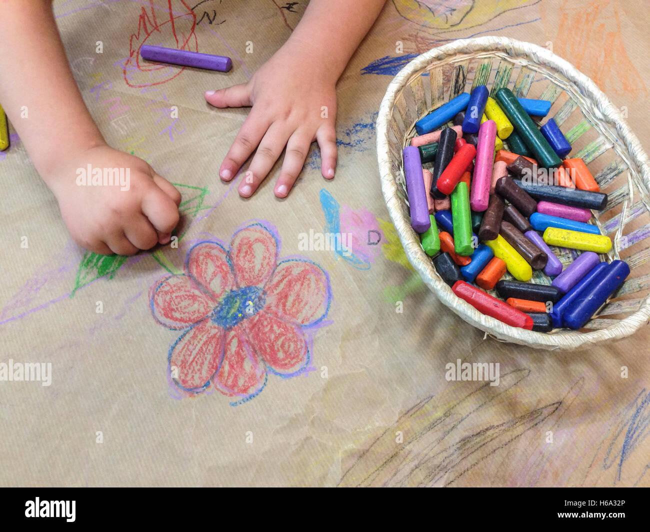 Dessin de l'enfant avec un panier de crayons de cire sur craft papier d'emballage. High angle view Banque D'Images