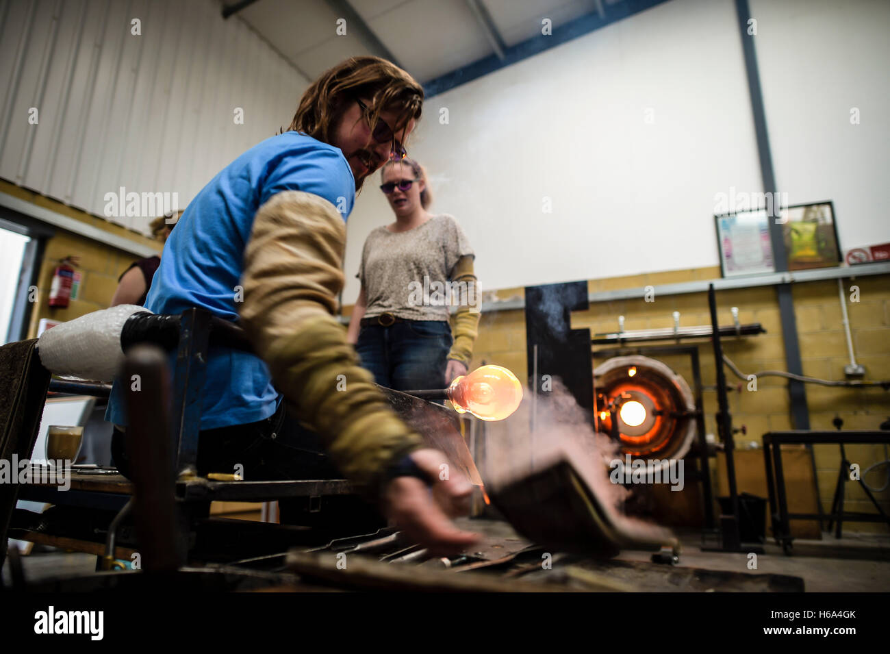 Souffleur de verre spécialiste James Devereux utilise journal humide de façonner un morceau de verre en fusion, assisté par Katherine, Huskie qu'il fait le verre clair cocardes pour une sculpture dans son atelier dans le Wiltshire. Banque D'Images