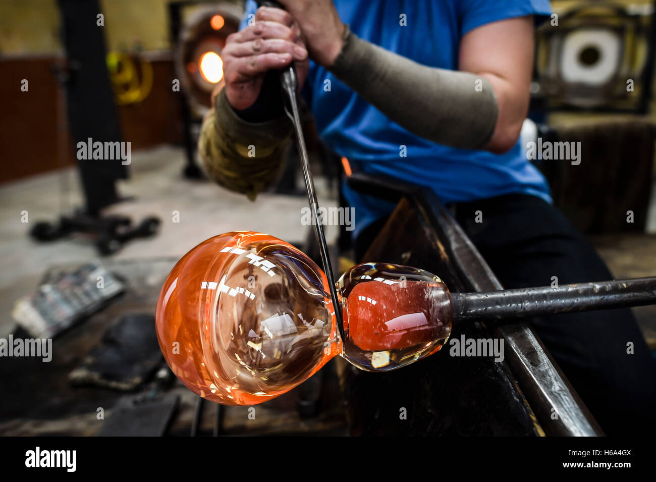Souffleur de verre spécialiste James Devereux utilise des étriers métalliques à façonner un morceau de verre en fusion qu'il fait le verre clair cocardes pour une sculpture dans son atelier dans le Wiltshire. Banque D'Images