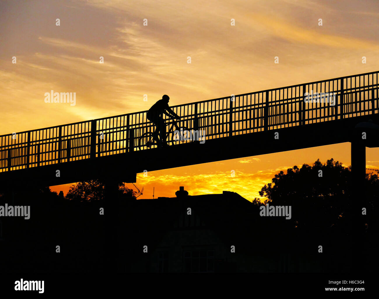 Personne en silhouette du vélo sur passerelle piétonne avec la couleur rempli Ciel de coucher du soleil derrière. Banque D'Images