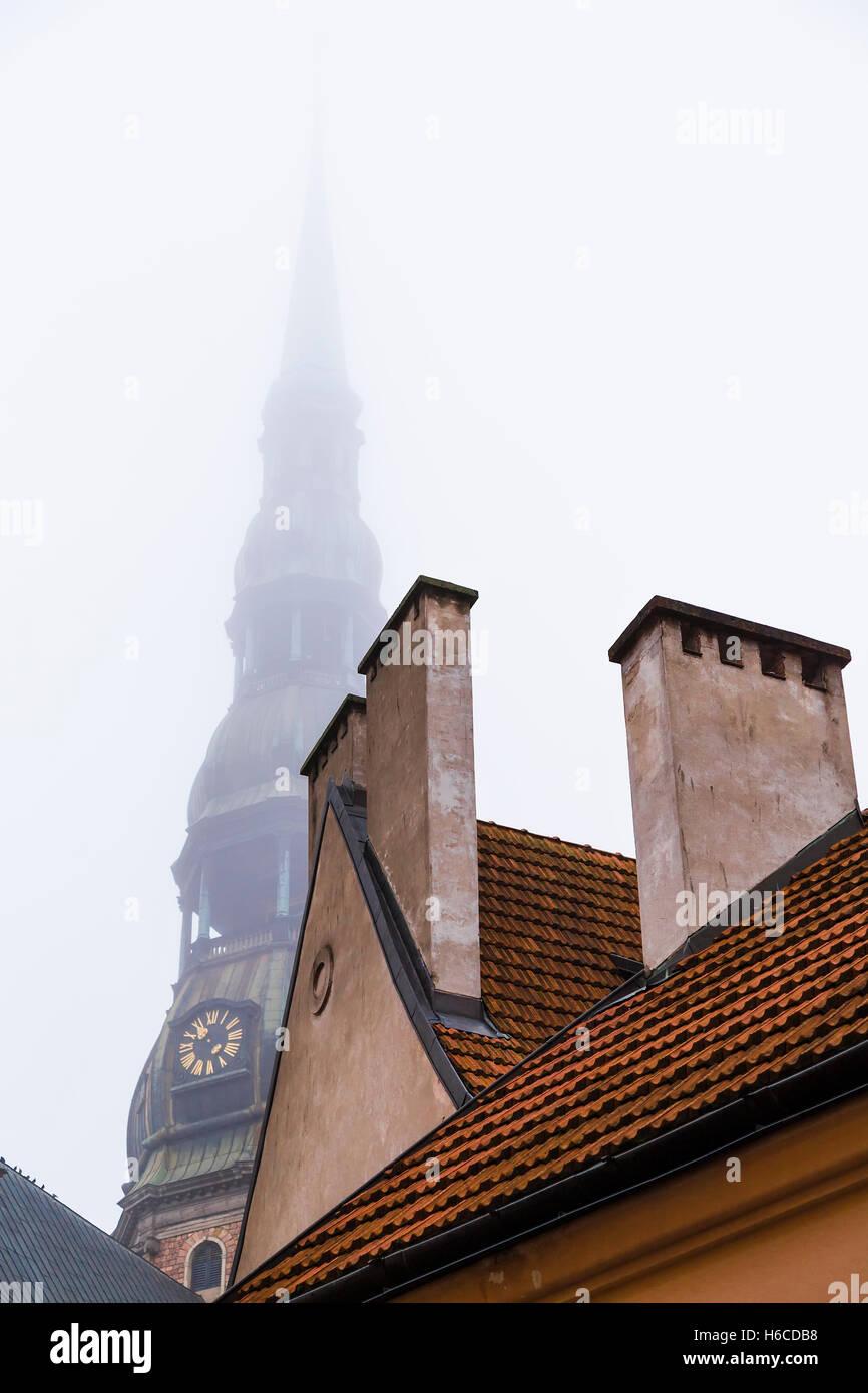 Tuiles du toit de la maison et la flèche de la cathédrale de Saint Pierre dans le brouillard. Riga. La Lettonie Banque D'Images