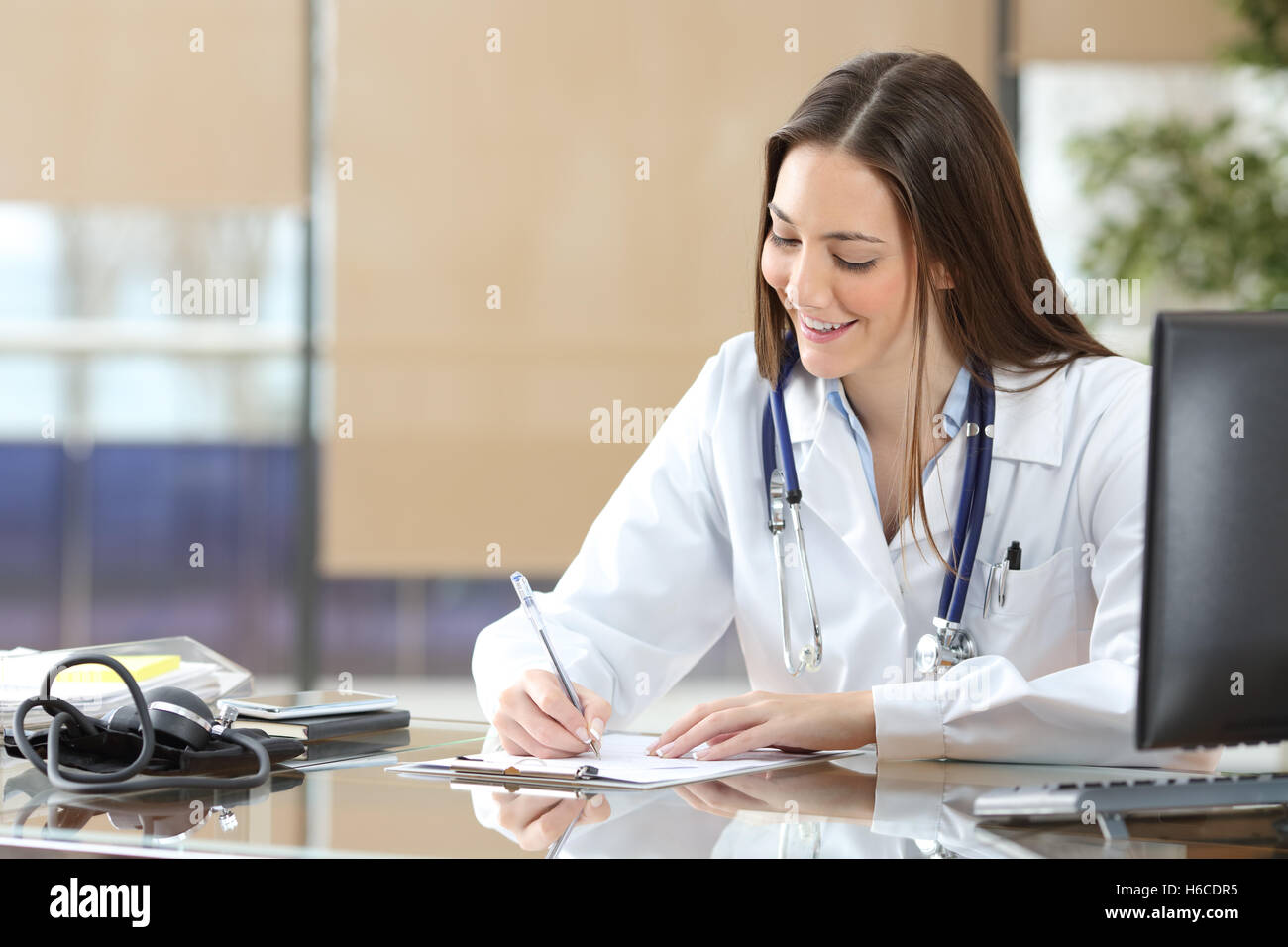 Médecin femme qui écrit dans une histoire médicale assis dans un bureau à la consultation Banque D'Images