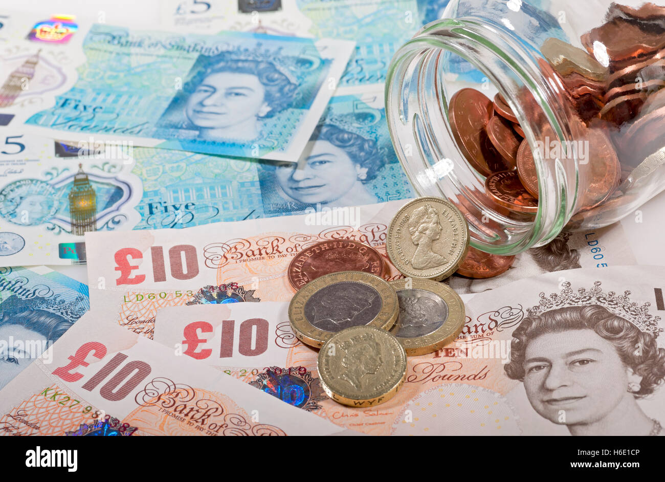 Gros plan de l'argent anglais polymère billets de cinq livres et pièces de monnaie se déversant d'un concept d'épargne de financement de pot Angleterre Royaume-Uni GB Grande-Bretagne Banque D'Images