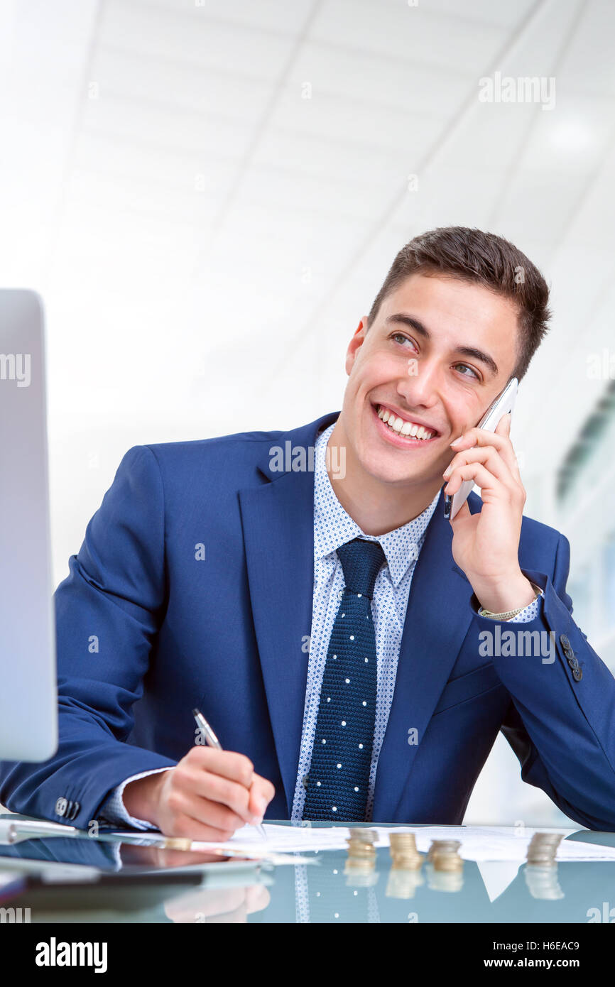 Close up portrait of handsome young businessman talking on smart phone in office. Jeune homme au bureau devant l'ordinateur. Banque D'Images