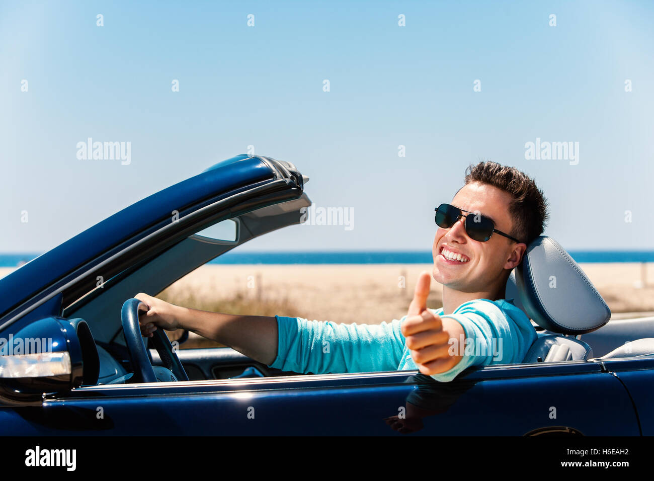 Portrait of attractive young man sitting in convertible bleu doing Thumbs up. Banque D'Images