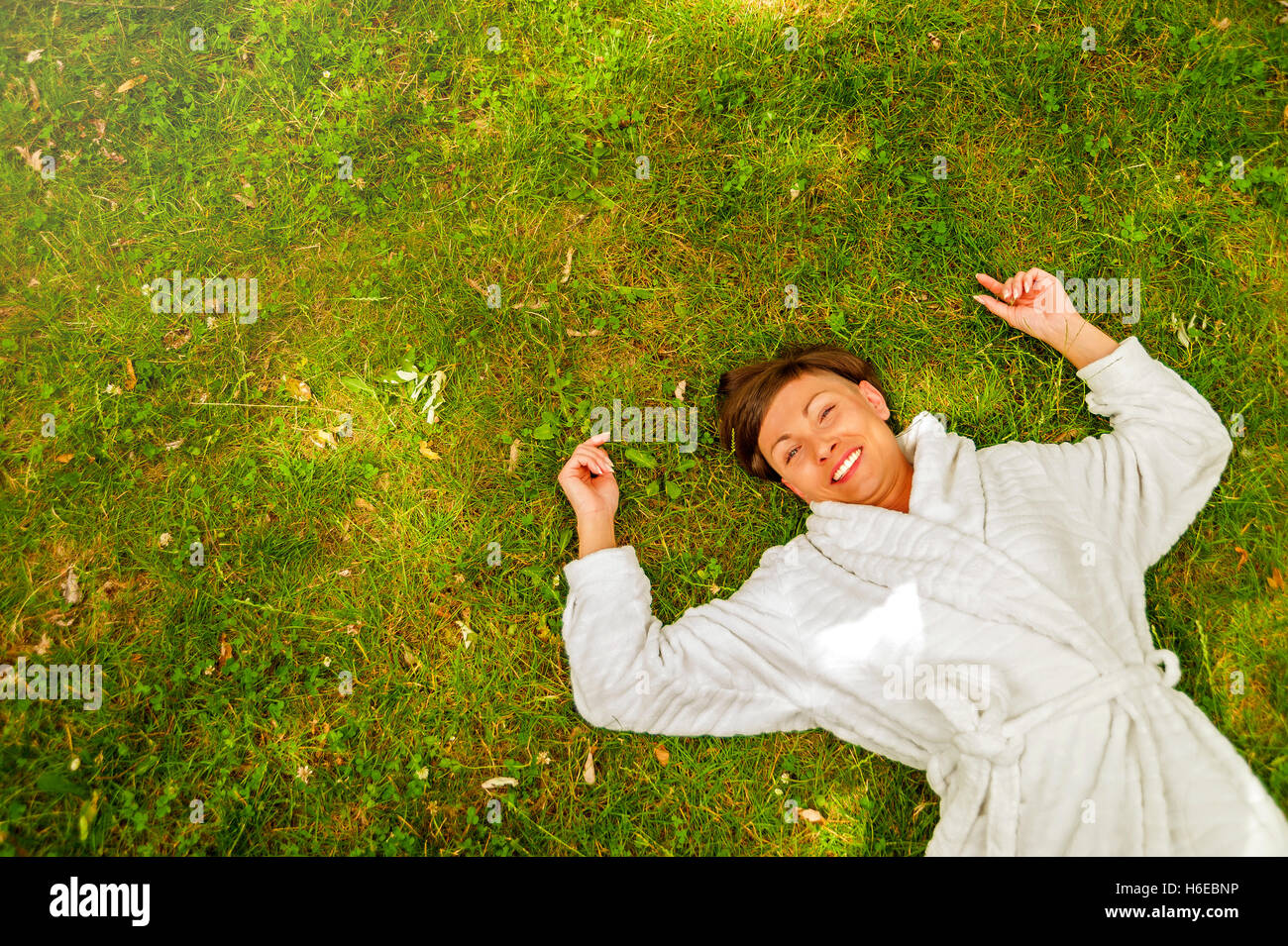 Happy laughing woman lying large arms in Green grass Banque D'Images