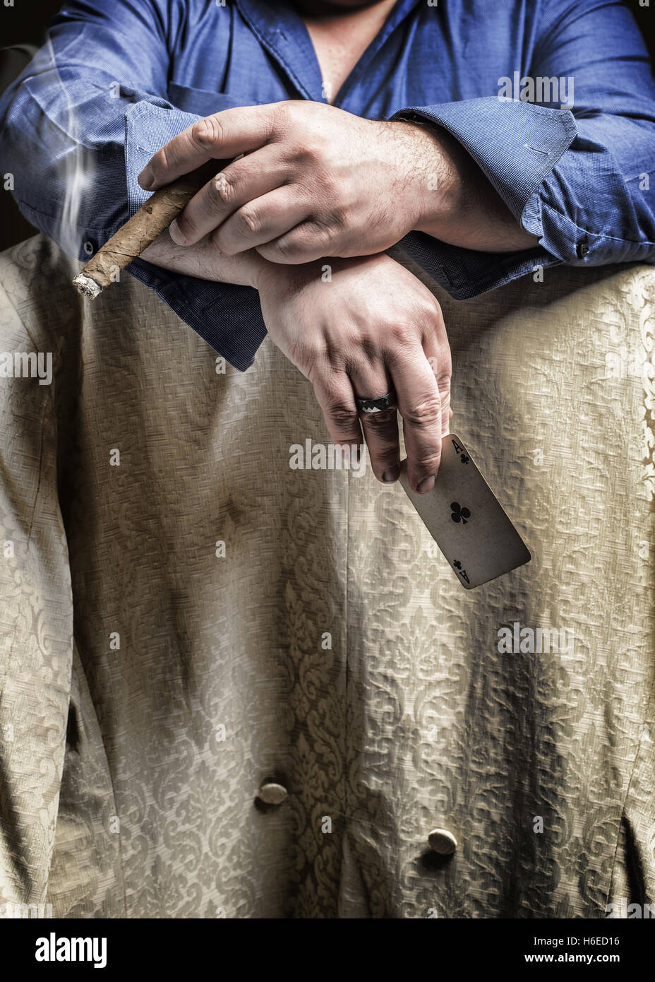 Homme assis à califourchon sur une chaise fumer un cigare et la tenue d'une carte à jouer Ace Banque D'Images