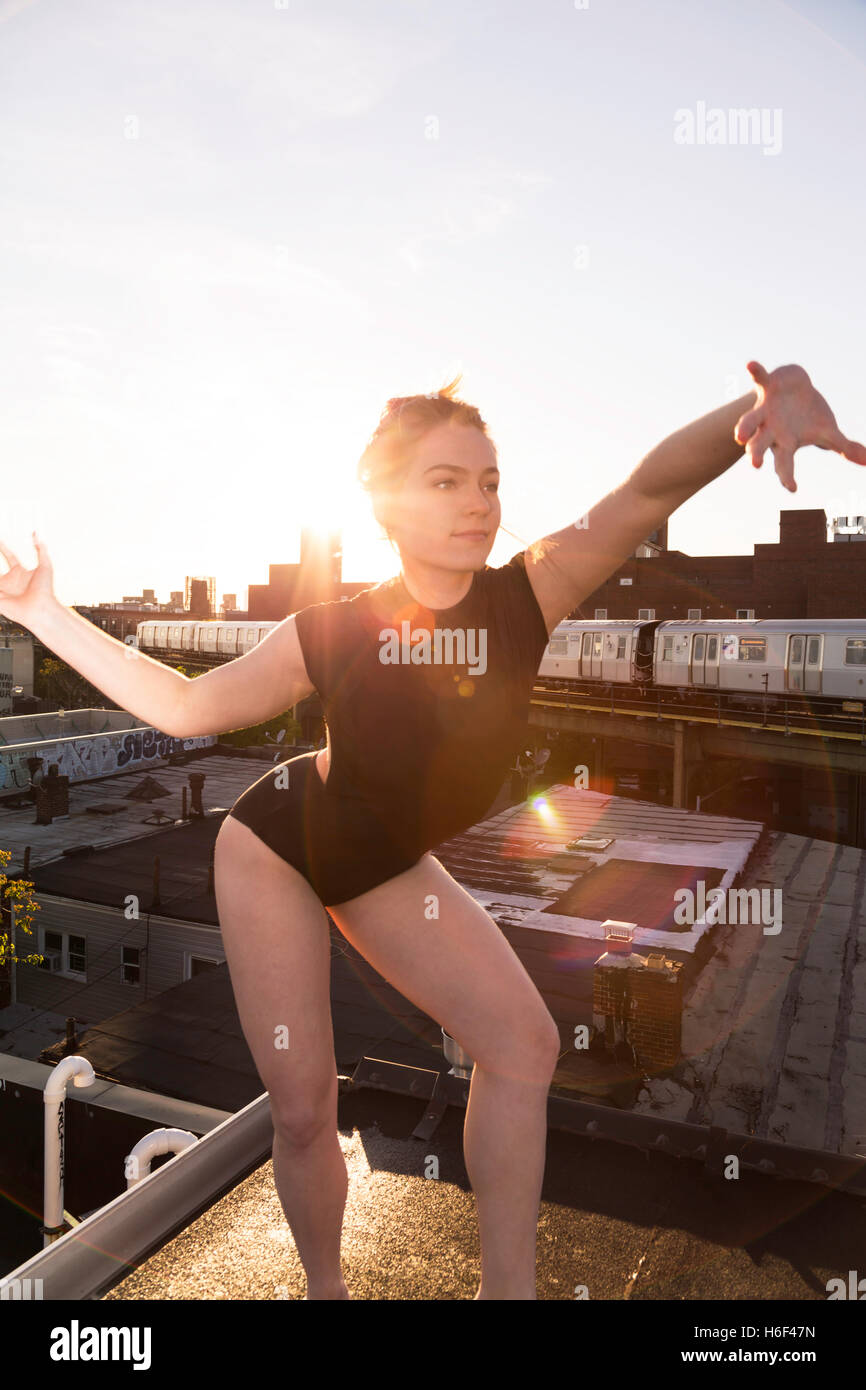 Une femme danse sur un toit-terrasse au coucher du soleil comme un métro train passe dans l'arrière-plan Banque D'Images
