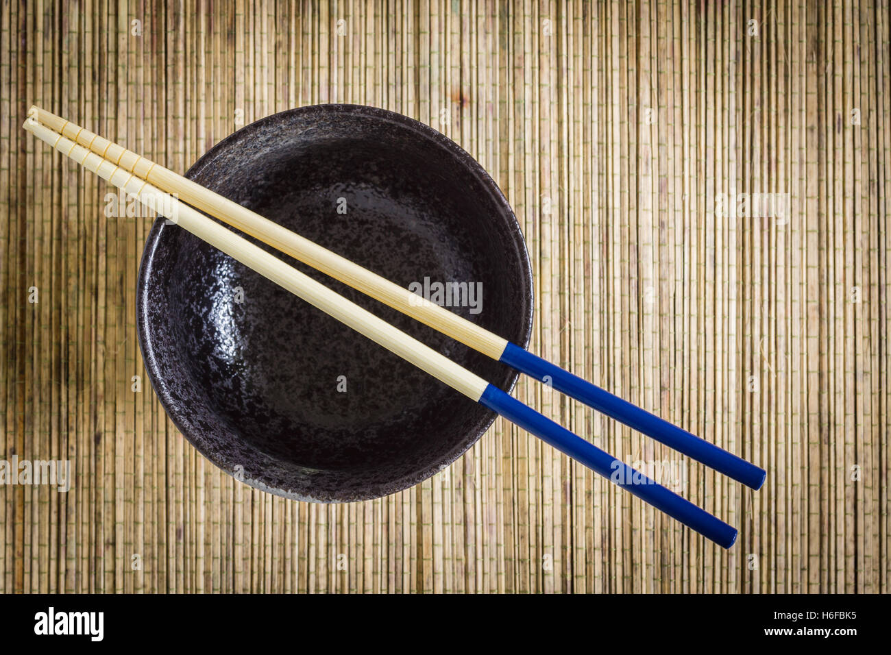 Baguettes et de riz ou de bol de nouilles contre un arrière-plan de nattes de bambou idéal pour les sujets de l'alimentation asiatique Banque D'Images