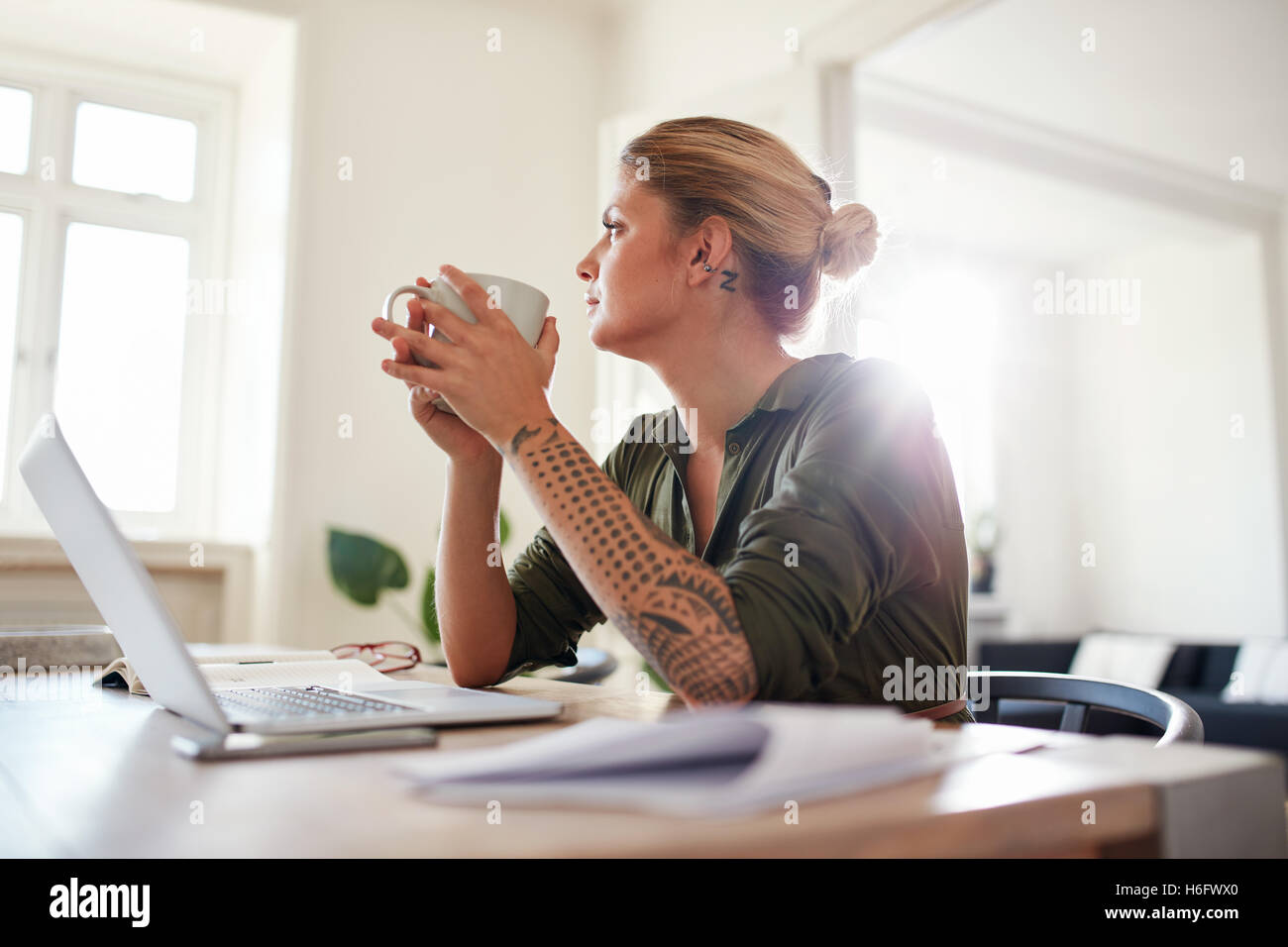Tourné à l'intérieur de la jeune femme avec du café à l'écart et la pensée. Femme sérieuse assis à votre bureau à domicile. Banque D'Images Tourné à l'intérieur de la jeune femme avec du café à l'écart et la pensée. Femme sérieuse assis à votre bureau à domicile. Banque D'Images